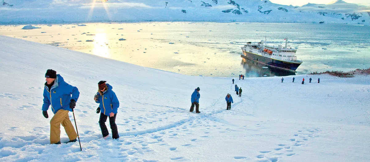 Travelers hiking up a snowy slope above an expedition ship in Antarctica