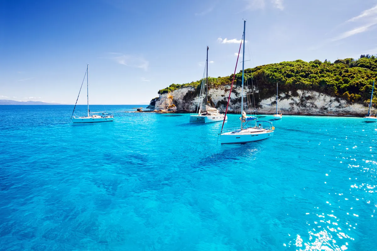 Sailboats anchored in a turquoise Greek cove