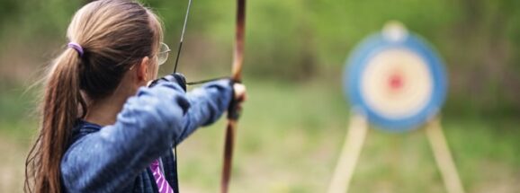 Teenage girl shooting bow at target in the forest